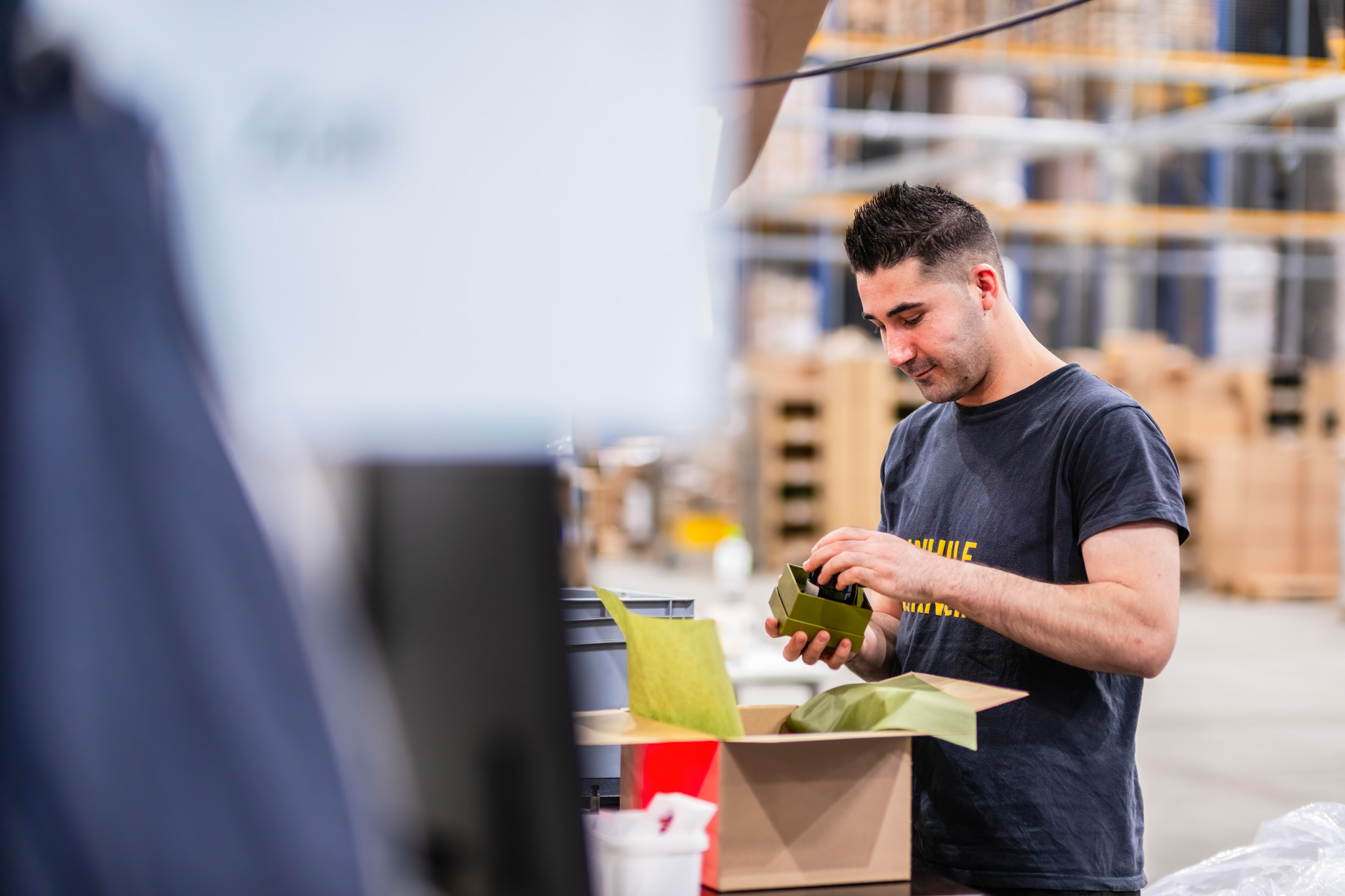 Ein Mitarbeiter der Versandmanufaktur bearbeitet einen Versandauftrag und befüllt ein Paket mit Ware